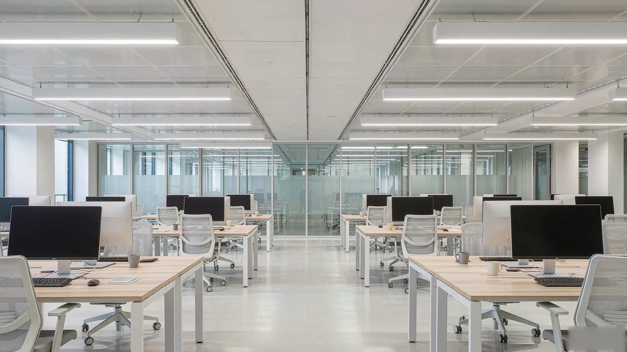 Open-plan office lit by even, low-glare linear LED luminaires.